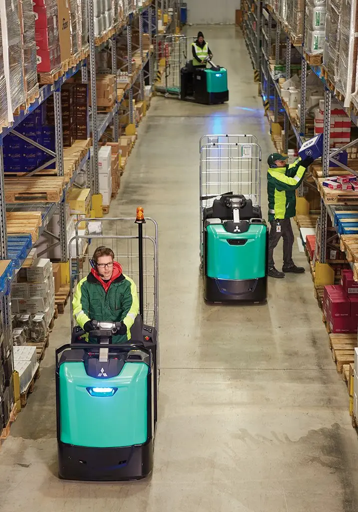 Tre lagermedarbetare i en lagergång med Logisnext pallyftare och orderplocktruckar, en plockar gods från hyllan medan de övriga kör