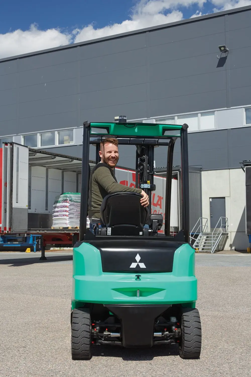 Leende förare i Mitsubishi motviktstruck framför lastbil vid lastningsramp – Logisnext