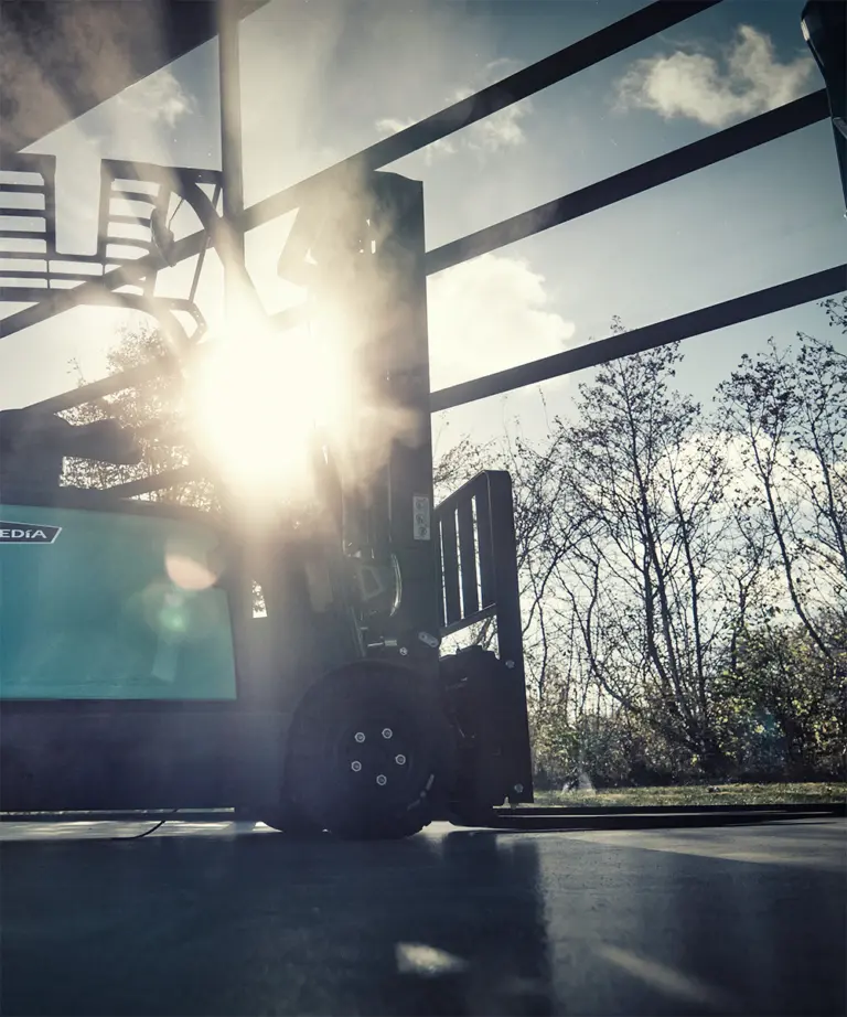 Mitsubishi Edia motviktstruck i motljus vid lagerport med solsken och träd i bakgrunden – Logisnext