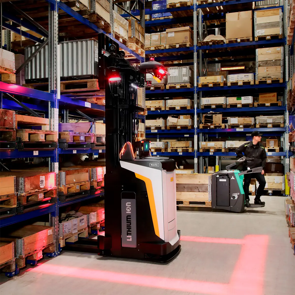 Autonom Rocla-truck med aktiverad rödljus säkerhetszon bredvid en lagerarbetare med palltruck