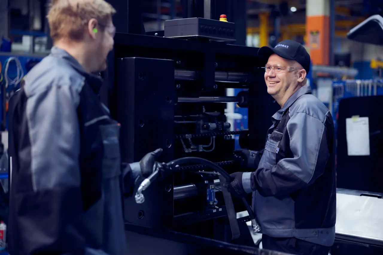 Leende Logisnext-montör kopplar hydraulslang på en trucks lyftmast tillsammans med en kollega