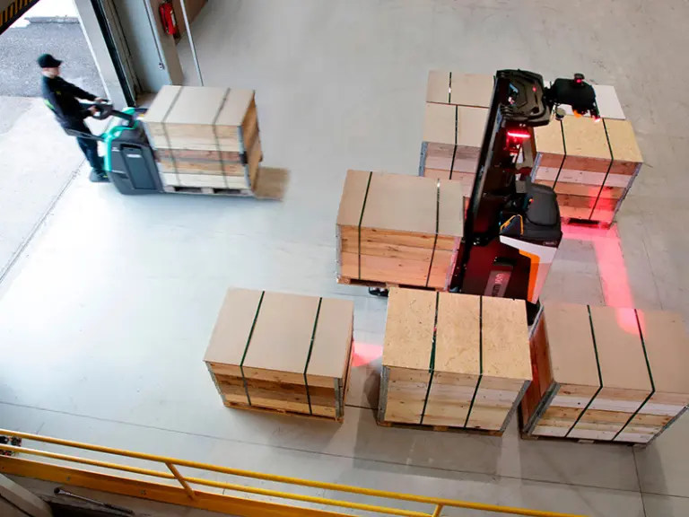 Uppifrånvy av lagermedarbetare med eldriven plocktruck och autonom truck med varningsljus bland packade kollin – Logisnext
