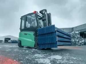 Logisnext EDiA eltruck på 3,5 ton med sluten hytt som transporterar blå stålbalkar utomhus på en isig industrigård