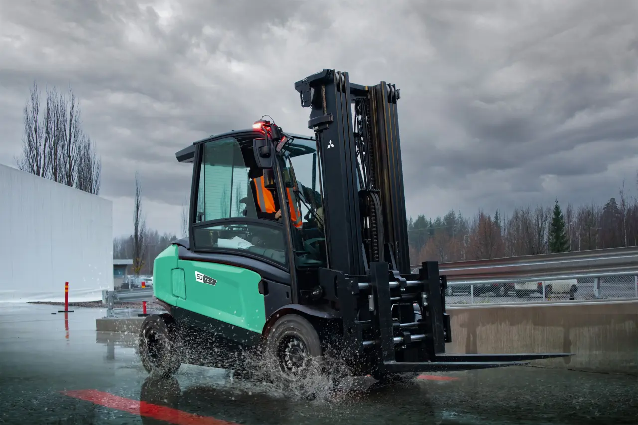 Logisnext EDiA eltruck på 5 ton med gaffelpositionerare som svänger i hög fart genom vattenpölar utomhus i regnväder