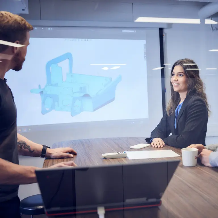 Kollegor i ett möte runt ett konferensbord med en 3D-modell av ett truckchassi projicerad på väggen