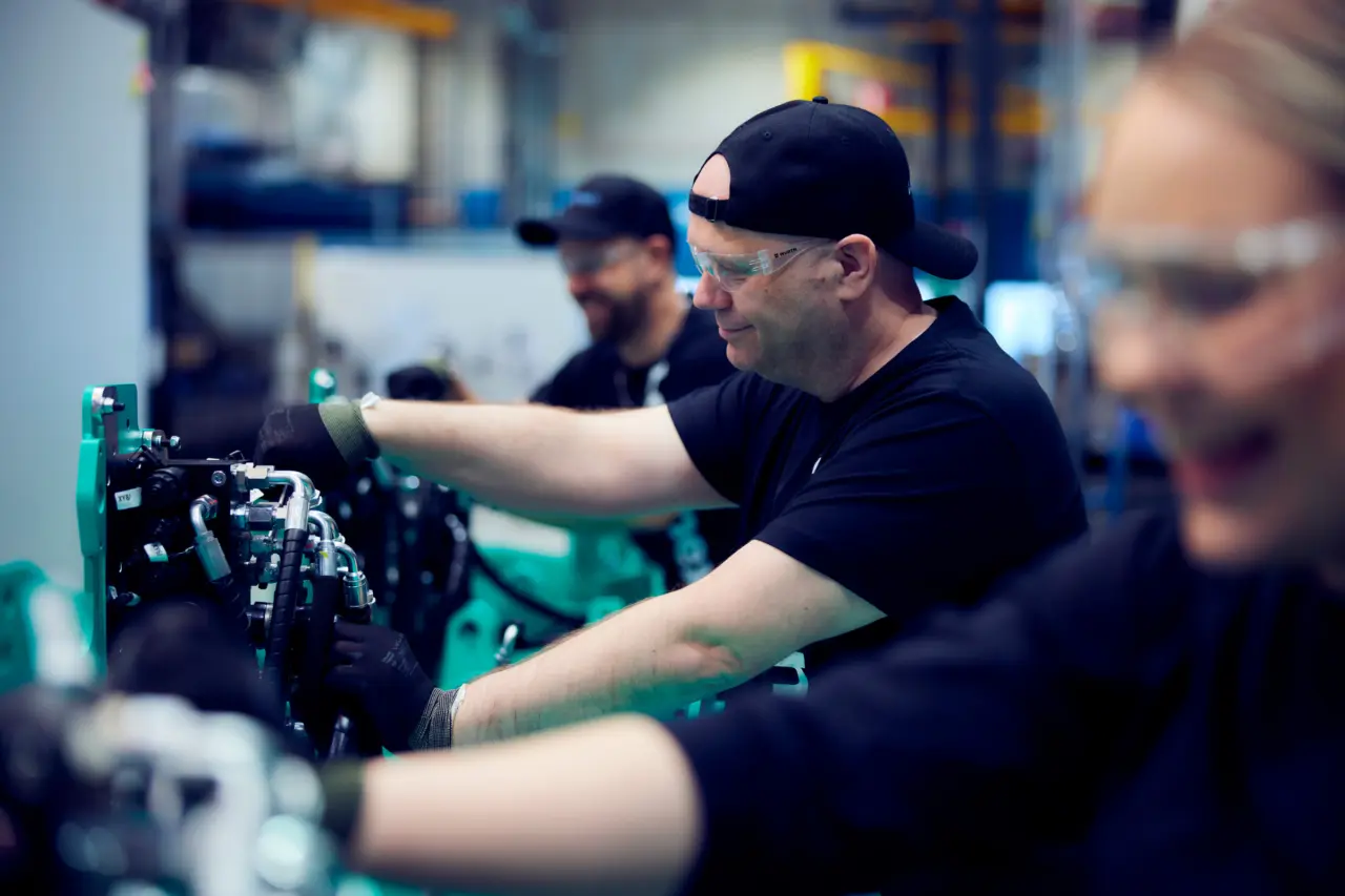 Montörer med skyddsglasögon arbetar med hydraulslangar på en industrimaskin i produktion